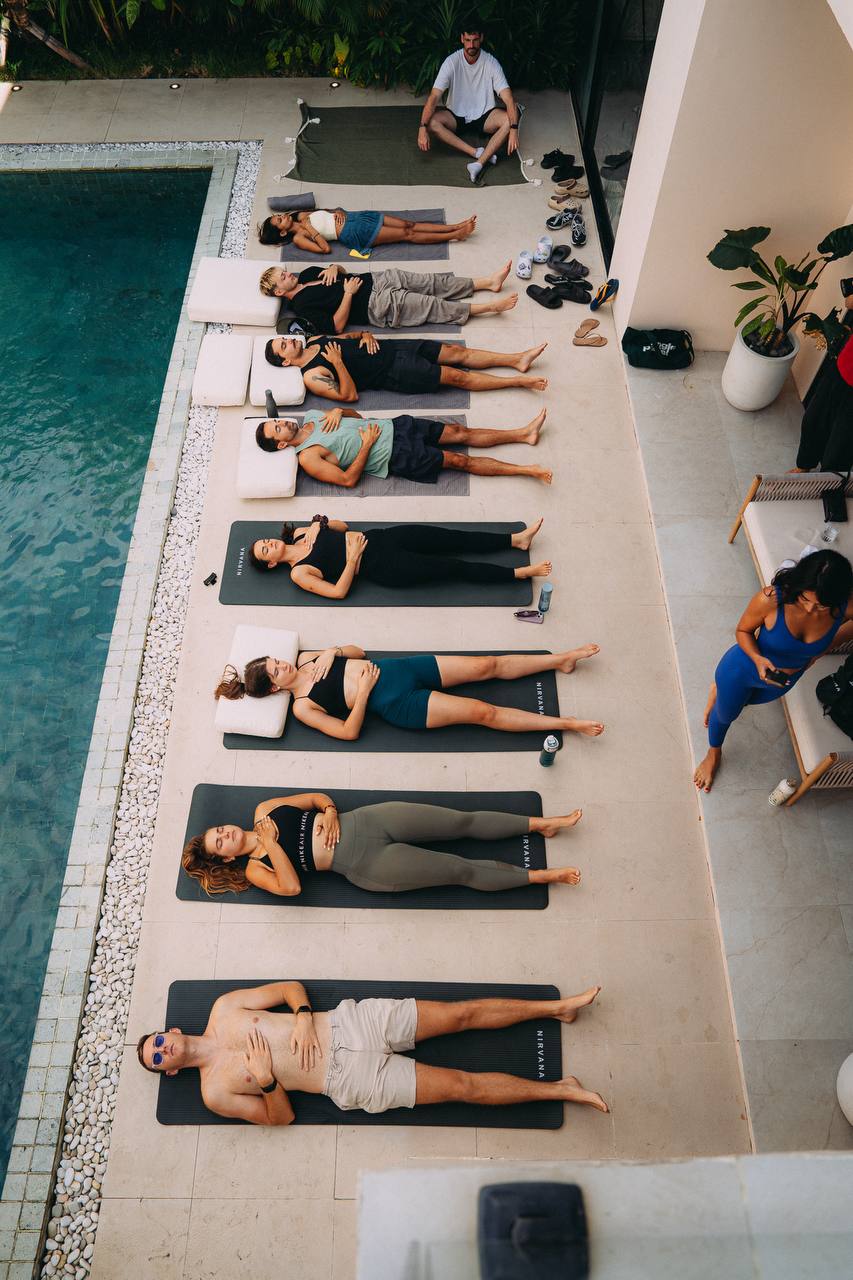 A group warming up on mats by the pool at an AcroByJoe session